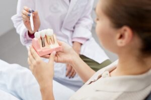 Woman holding dental implant model while dentist explains. 