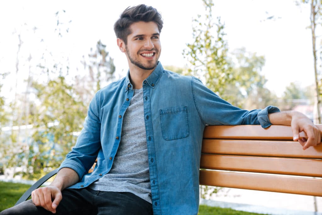 Handsome,Young,Man,Sitting,On,A,Bench,Smiling,In,The